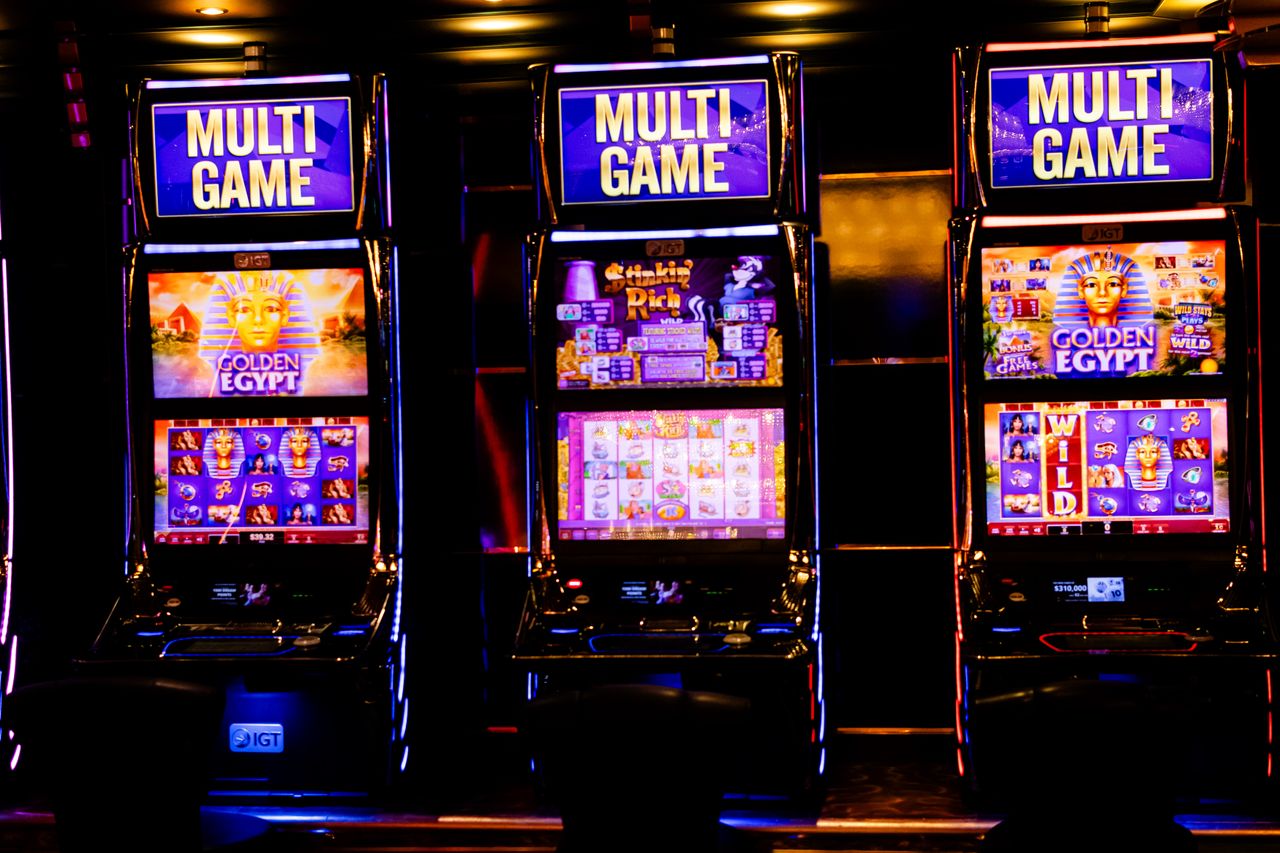 services-01 Three illuminated slot machines in a bustling casino at night.