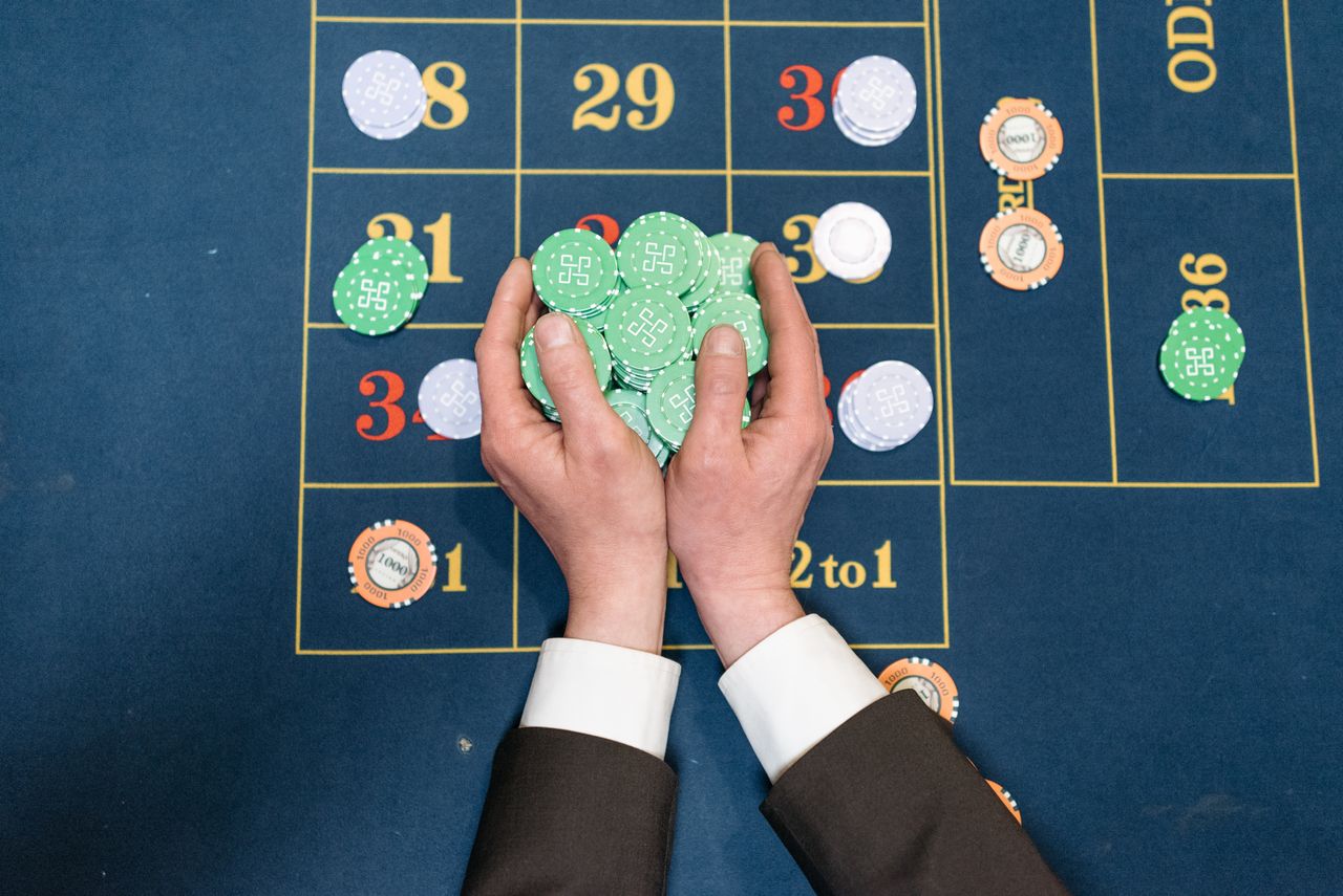 our-services-1 Hands in a suit holding poker chips on a casino gaming table.