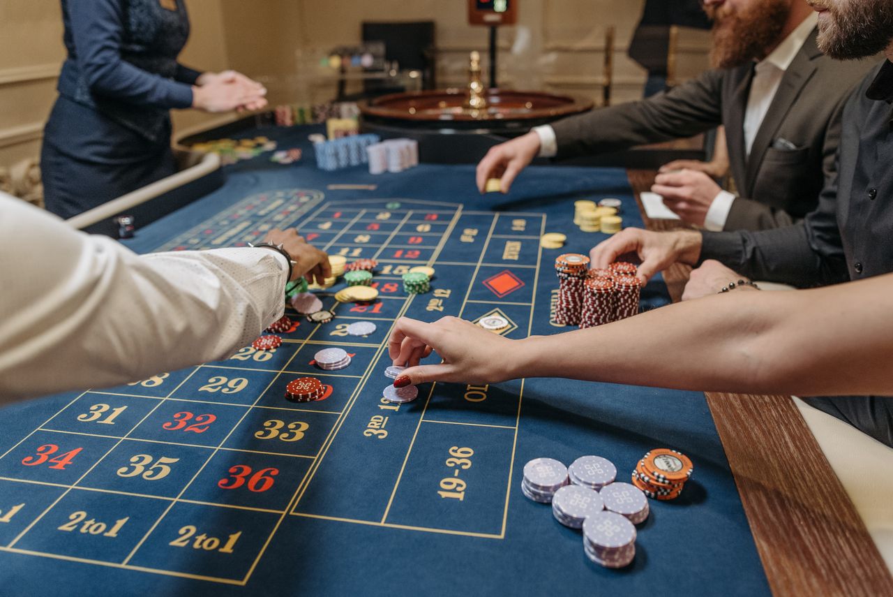 about-01 A lively casino scene with players placing bets and handling gaming chips on a roulette table.
