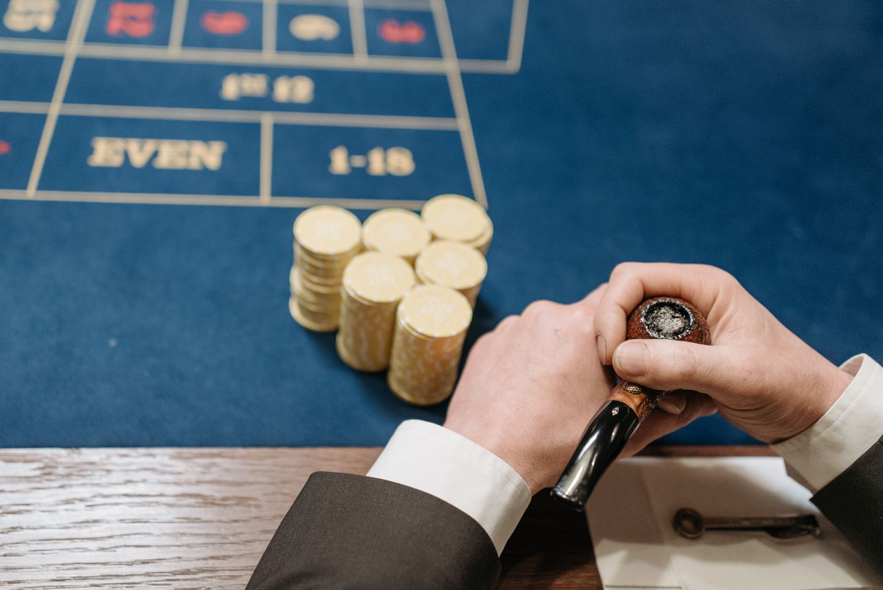 gallery-1 Hands holding a tobacco pipe and poker chips on a casino table. Top view.